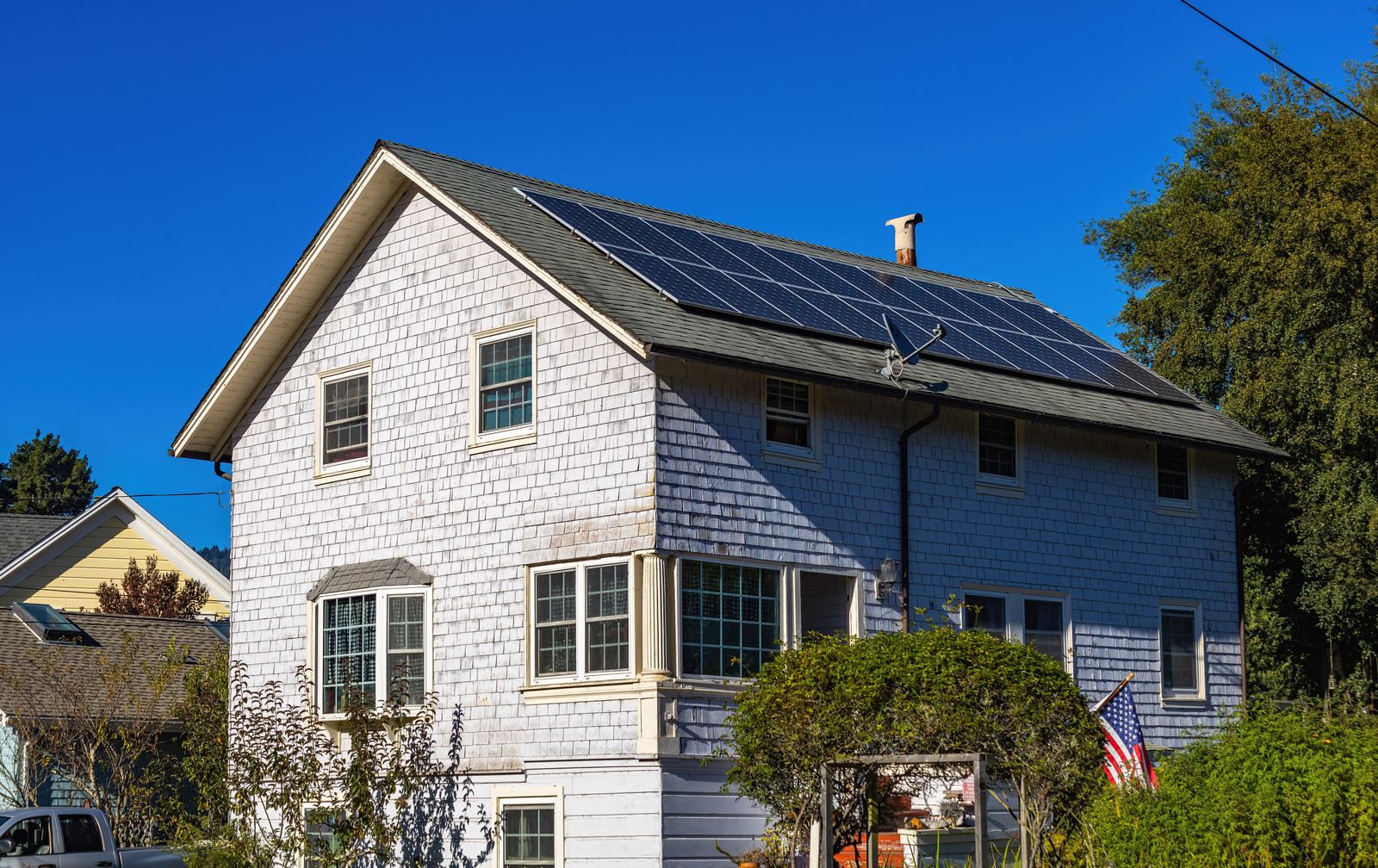 A modern two-story home with solar panels on its roof under a clear blue sky.